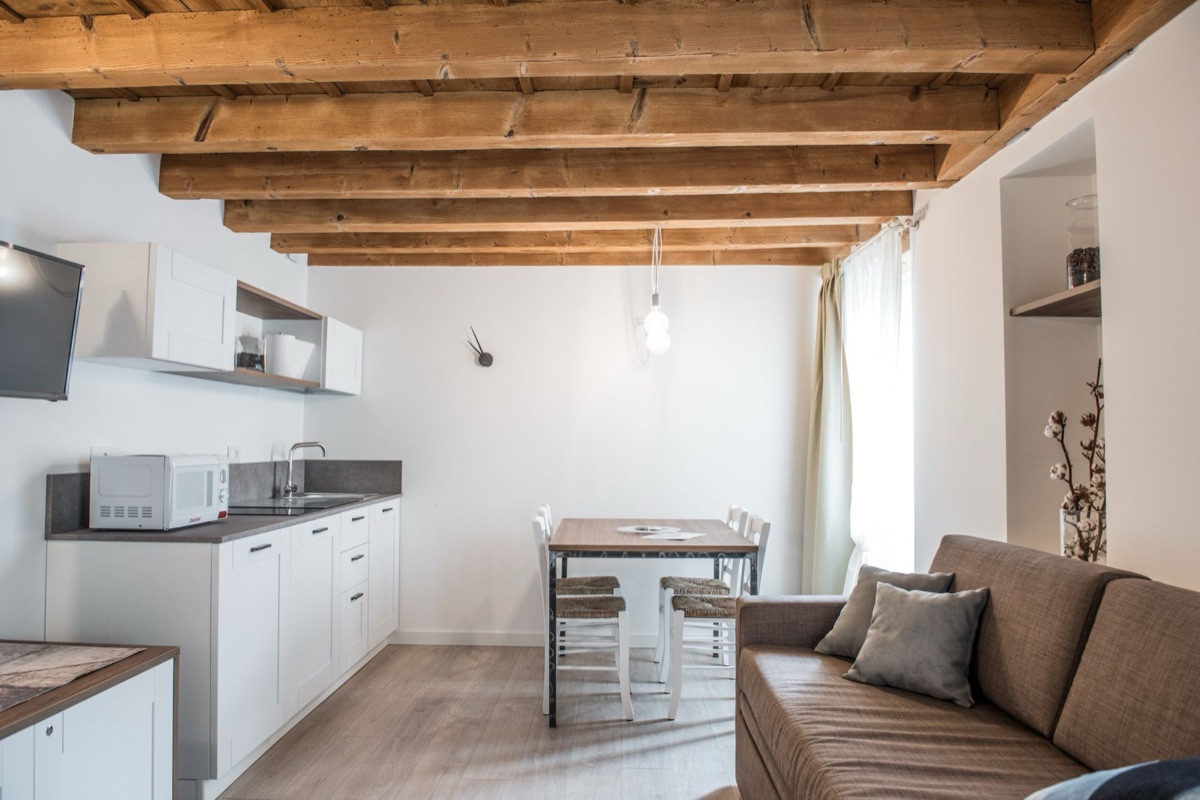 Open space con cucina bianca, tavolo, divano e soffitto a travi in legno
