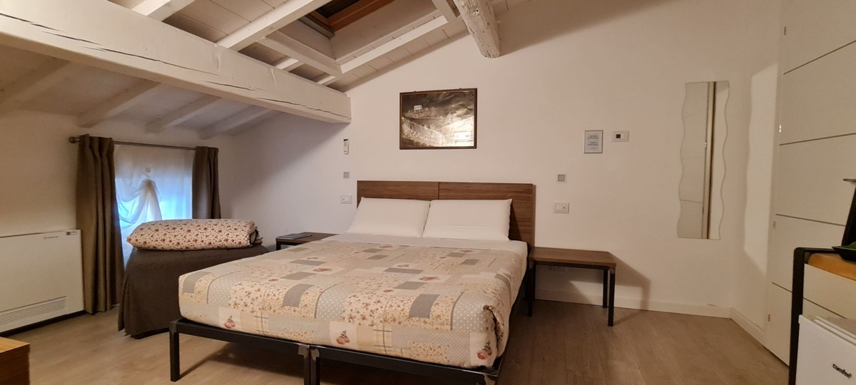 Vista panoramica della camera con letto matrimoniale, letto aggiunto e quadri