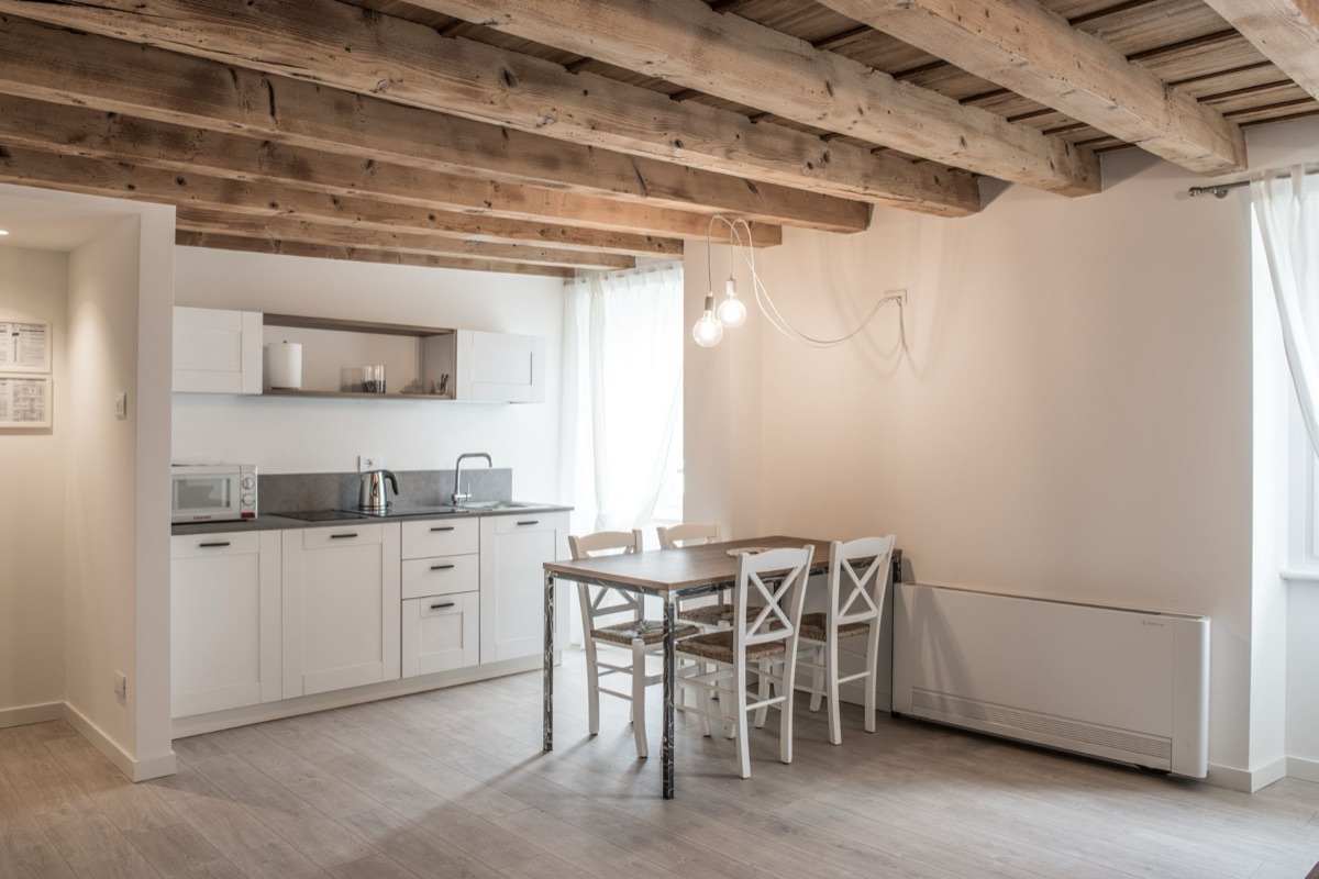 Cucina bianca e tavolo da pranzo sotto un soffitto di travi in legno chiaro